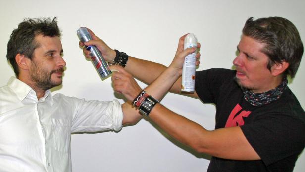 Zwei Männer halten sich gegenseitig mit Haarspraydosen auf Abstand.