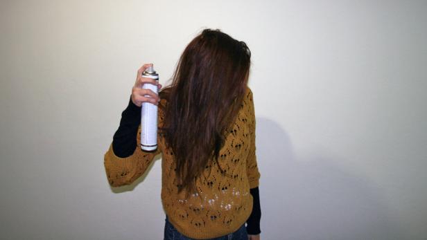 Eine Frau sprüht Haarspray in ihr Haar.