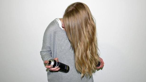 Eine Frau sprüht sich Haarspray in die langen, blonden Haare.