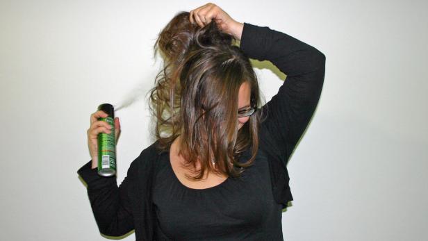 Eine Frau fixiert ihre Frisur mit Haarspray.