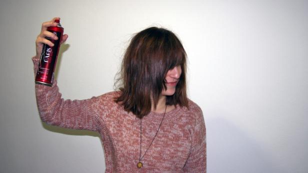 Eine Frau sprüht sich Haarspray der Marke „Paris“ in die Haare.