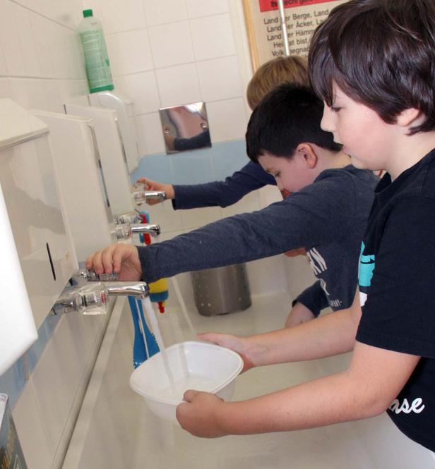 Drei Jungen stehen an einem Waschbecken und füllen Wasser in eine Schüssel.