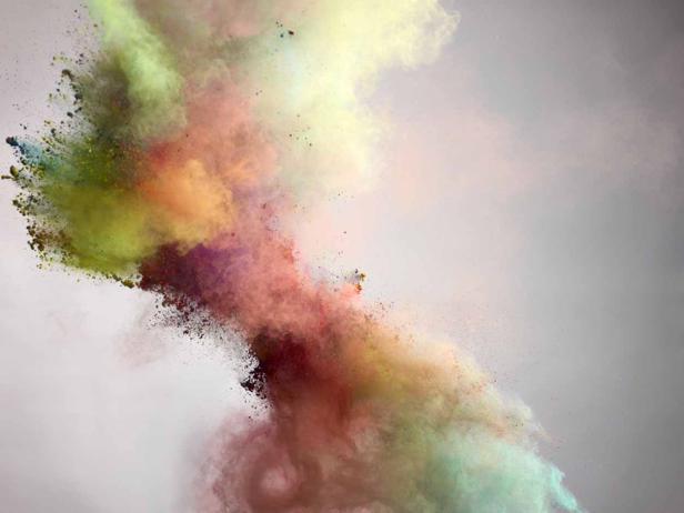Eine Explosion aus buntem Farbpulver vor einem grauen Hintergrund.