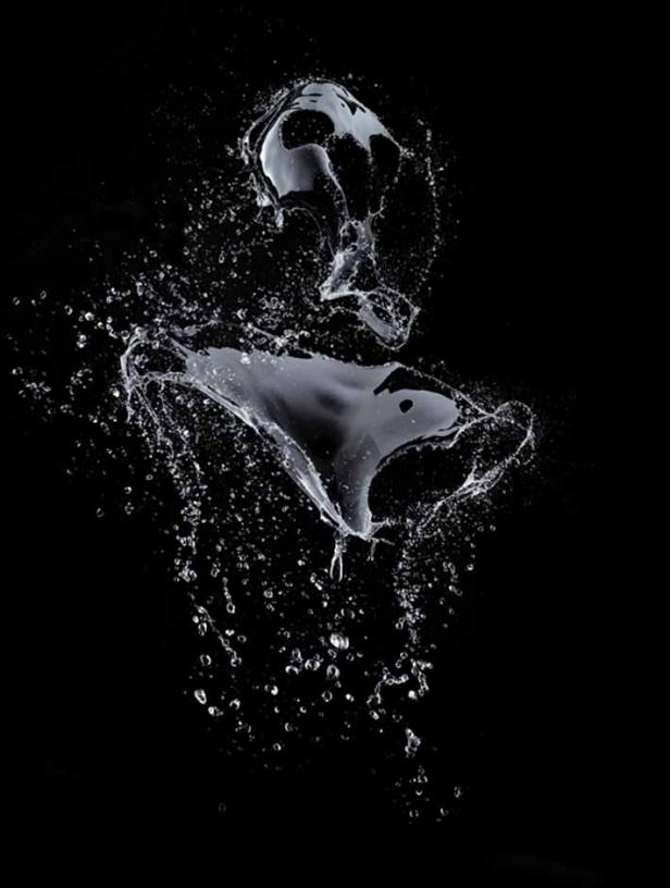 Wassertropfen und Spritzer erstarren in der Luft vor einem schwarzen Hintergrund.