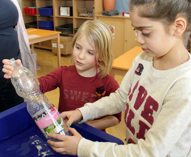 Zwei Mädchen untersuchen eine Plastikflasche in einem blauen Behälter.