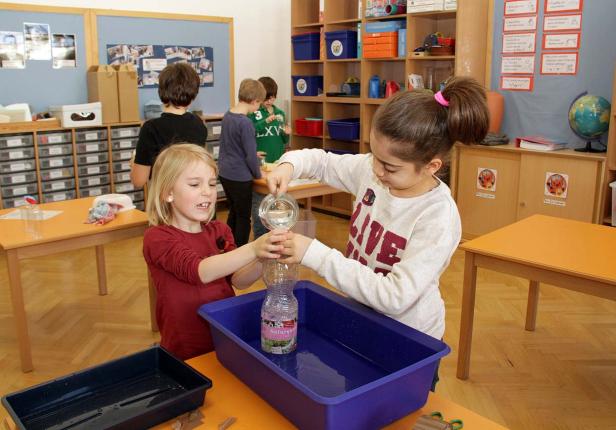 Zwei Mädchen experimentieren mit Wasser und einer Plastikflasche in einem Klassenzimmer.
