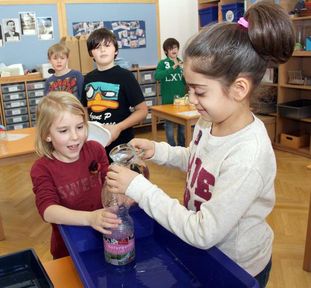Zwei Mädchen experimentieren im Klassenzimmer mit Wasser und einer Plastikflasche.