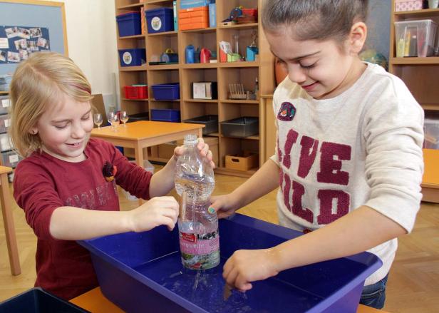 Zwei Mädchen spielen mit einer Wasserflasche in einer blauen Wanne.