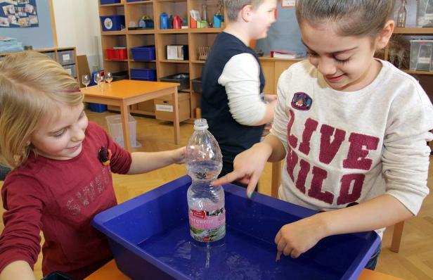 Zwei Mädchen experimentieren mit einer Wasserflasche in einer blauen Wanne.