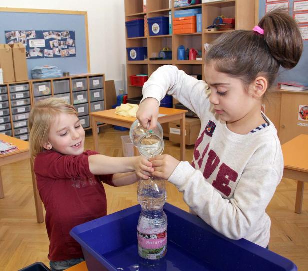 Zwei Mädchen experimentieren mit Wasser und einer Plastikflasche in einem Klassenzimmer.