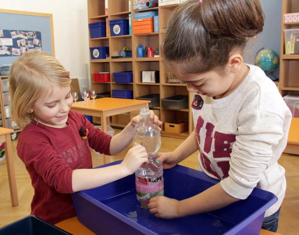 Zwei Mädchen experimentieren mit einer Wasserflasche in einer blauen Wanne.