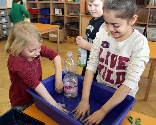 Zwei Mädchen spielen mit Wasser in einer blauen Wanne, in der eine Wasserflasche steht.