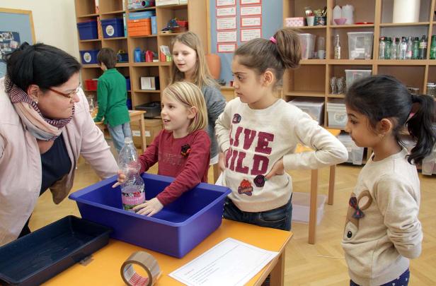 Eine Lehrerin erklärt einer Gruppe von Grundschulkindern ein Experiment mit einer Wasserflasche.
