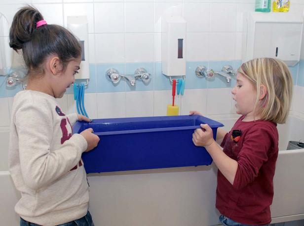 Zwei Mädchen tragen gemeinsam eine blaue Wanne in einem Badezimmer.