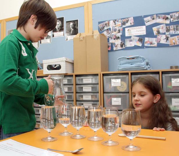 Ein Junge gießt Wasser in Gläser, während ein Mädchen zusieht.