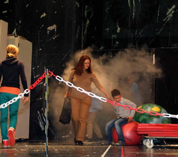 Auf einer Bühne interagieren Personen mit Requisiten und Ketten im Nebel.
