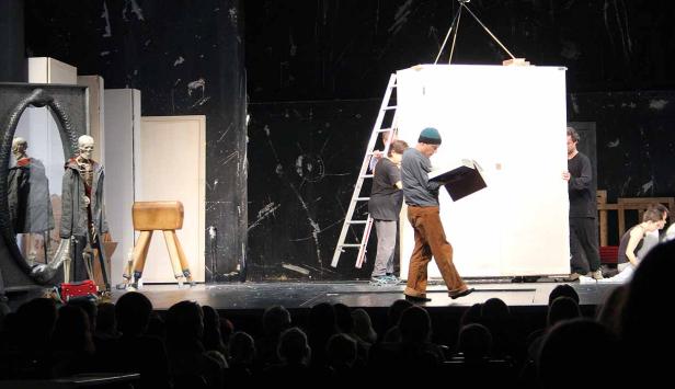 Eine Theaterszene mit Schauspielern, Requisiten und einem Publikum.