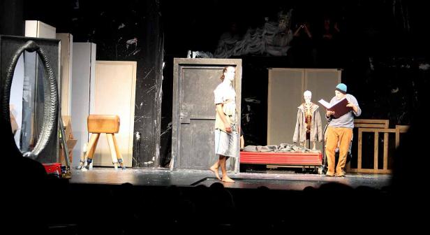 Eine Theaterszene mit Schauspielern und Requisiten auf einer Bühne.