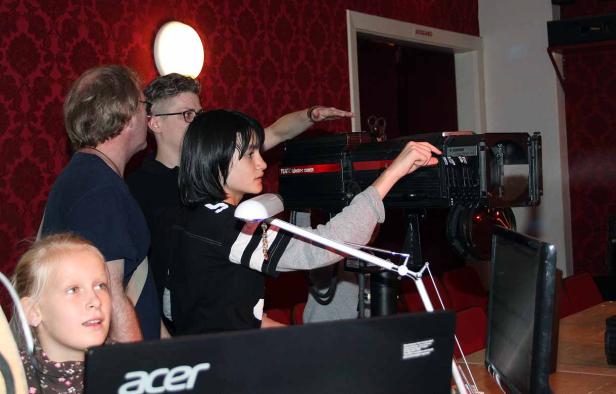 Eine junge Frau bedient eine große Theaterleuchte, umgeben von Zuschauern.