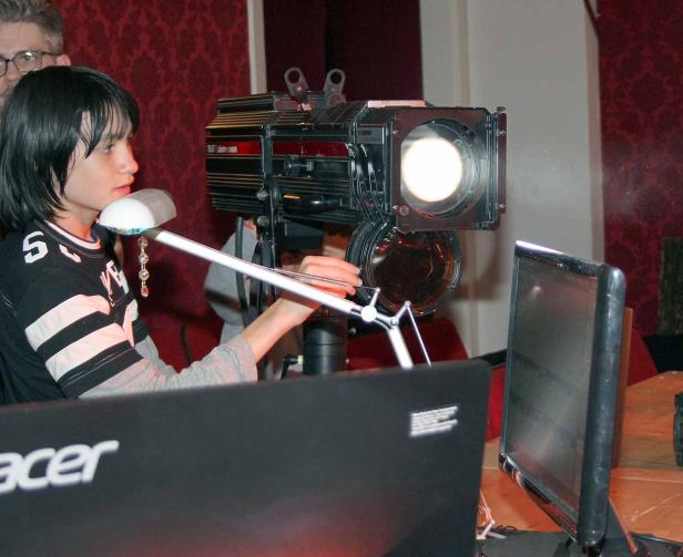 Eine Person bedient eine große Studioleuchte vor einem Laptop und einem Monitor.