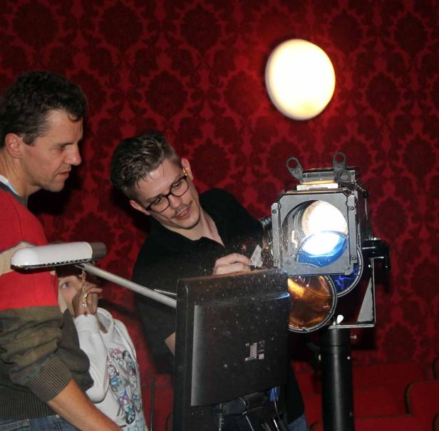 Zwei Männer richten einen Scheinwerfer vor einer roten Wand ein.