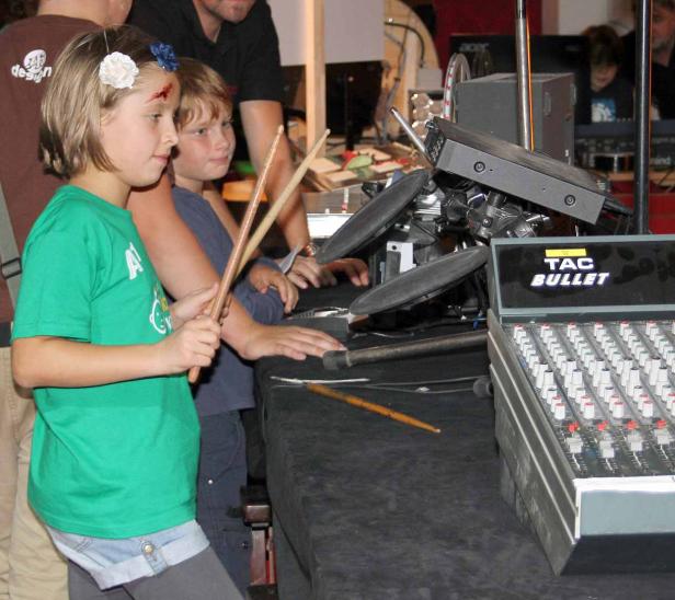 Zwei Kinder stehen mit Drumsticks an einem elektronischen Schlagzeug.
