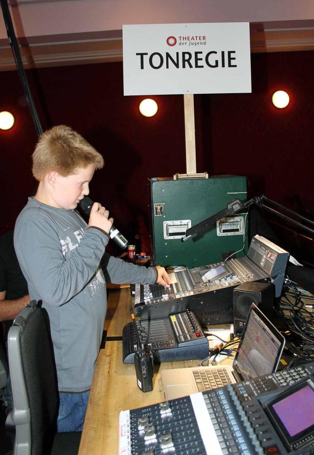 Ein Junge steht vor einem Mischpult und spricht in ein Mikrofon.