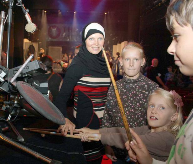 Eine Frau mit Hijab und Kinder stehen an einem elektronischen Schlagzeug.