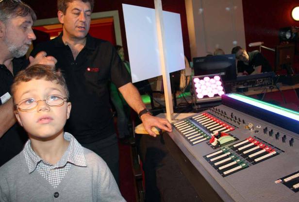 Ein Junge steht vor einem Mischpult, umgeben von zwei Männern.