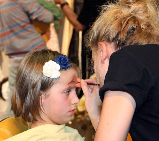 Ein Mädchen bekommt mit einem Pinsel eine Wunde auf die Stirn geschminkt.