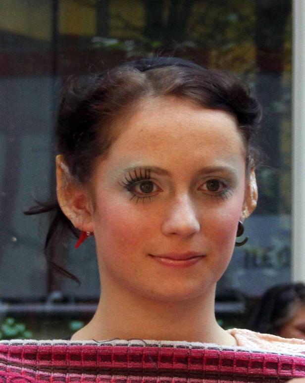 Eine junge Frau mit hellem Teint und auffälligem Make-up lächelt.