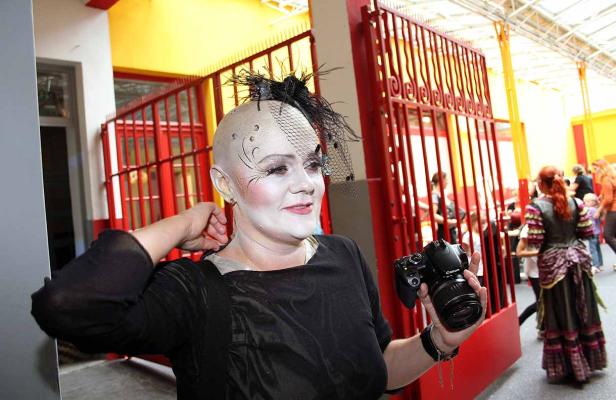 Eine Frau mit weiß geschminktem Gesicht und Kopf hält eine Kamera in der Hand.