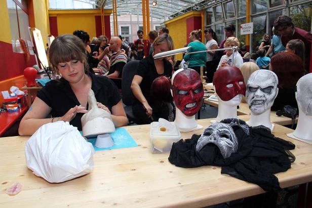 Eine Frau arbeitet an einer Maske, während im Hintergrund weitere Masken aufgereiht sind.