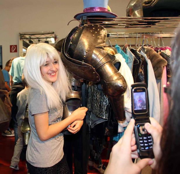 Ein Mädchen mit weißer Perücke posiert neben einer Ritterrüstung vor einem Kleiderständer.