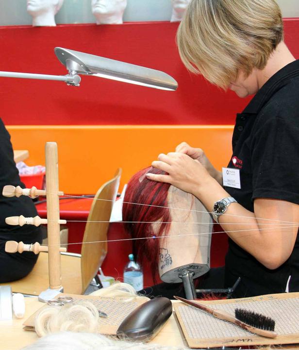 Eine Frau arbeitet an einer roten Perücke auf einem Übungskopf.