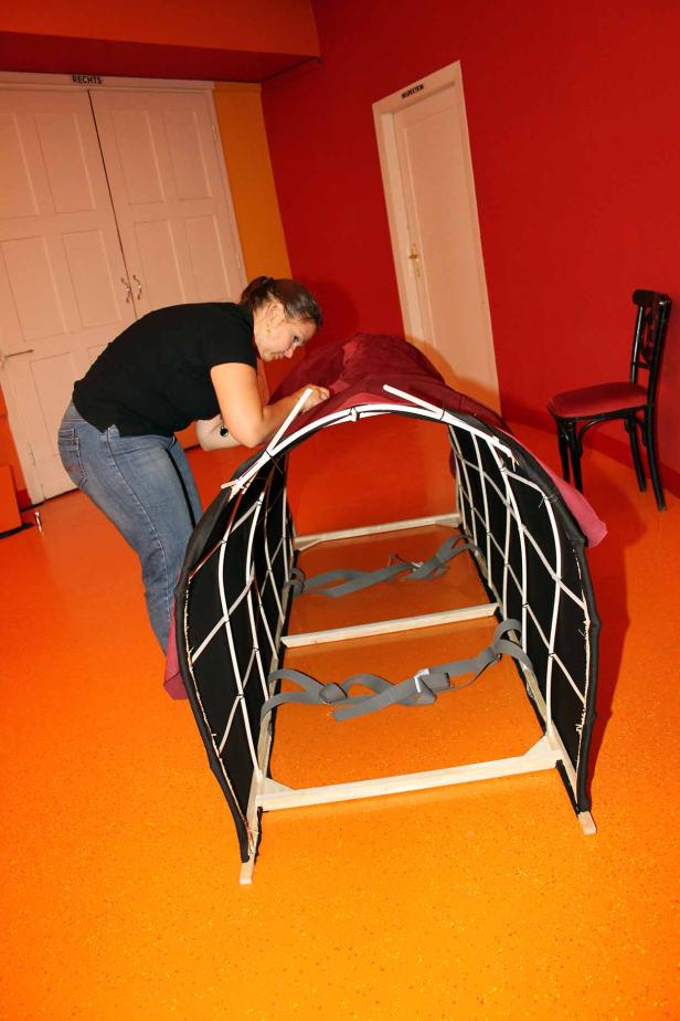 Eine Frau beugt sich über eine Art Liege mit einem schwarzen Netz und roten Stoffbezug.