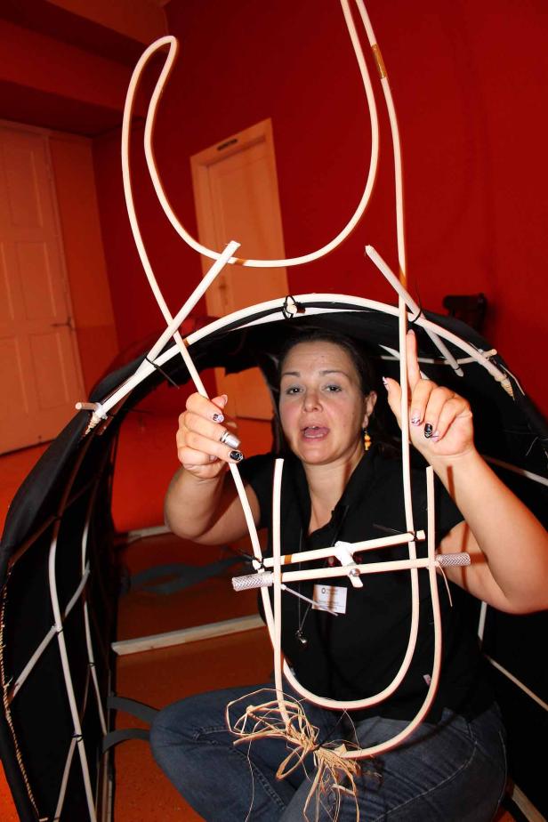 Eine Frau hockt in einem Raum und arbeitet an einer Konstruktion aus Stäben und Stoff.