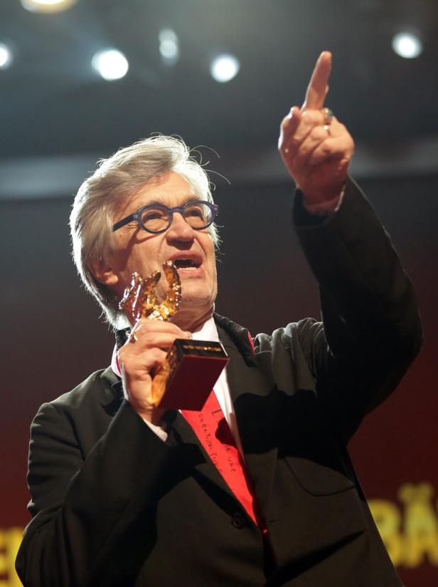 Ein Mann mit Brille hält eine goldene Trophäe und zeigt mit dem Finger nach oben.