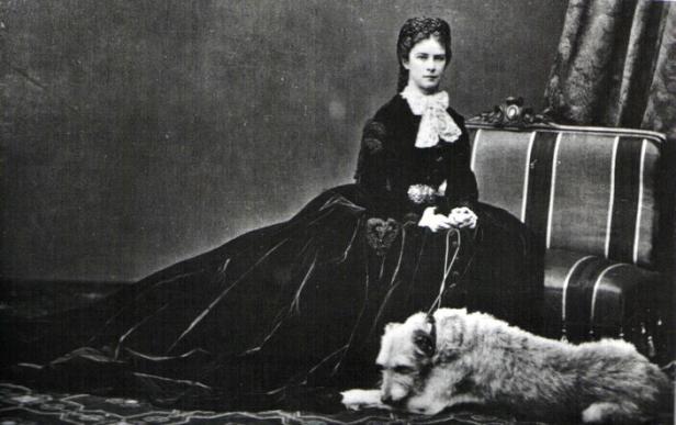 Kaiserin Elisabeth von Österreich sitzt mit ihrem Hund auf einem Sofa.