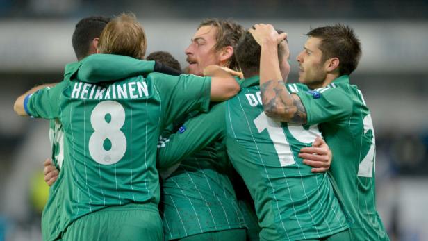 Mehrere Fußballspieler in grünen Trikots umarmen sich auf dem Spielfeld.