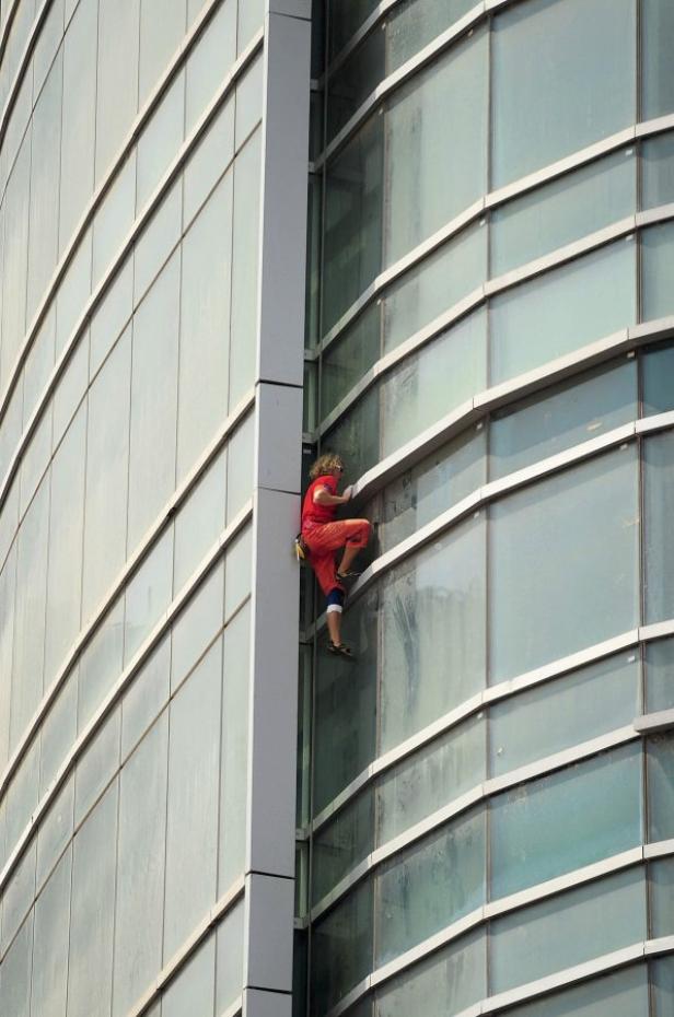 Eine Frau klettert an der Fassade eines modernen Bürogebäudes hoch.