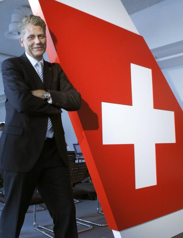 Ein Mann im Anzug steht neben einem großen Schweizerkreuz.