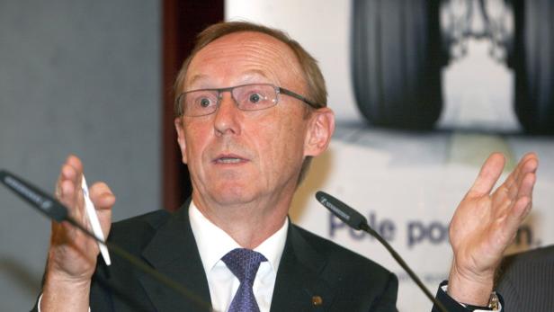 Ein Mann mit Brille gestikuliert bei einer Präsentation vor Mikrofonen.