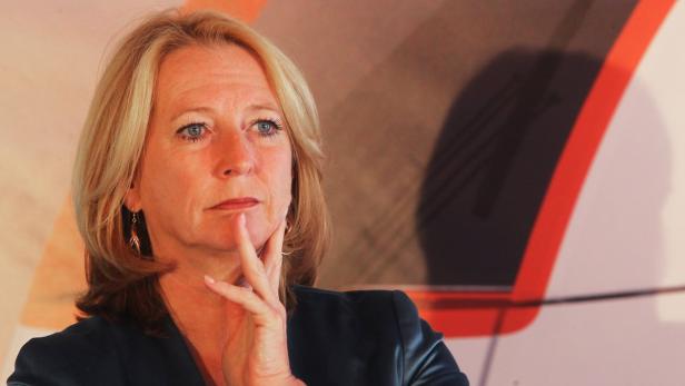 Eine Frau mit blonden Haaren und blauem Blick, die nachdenklich ihre Hand ans Kinn hält.