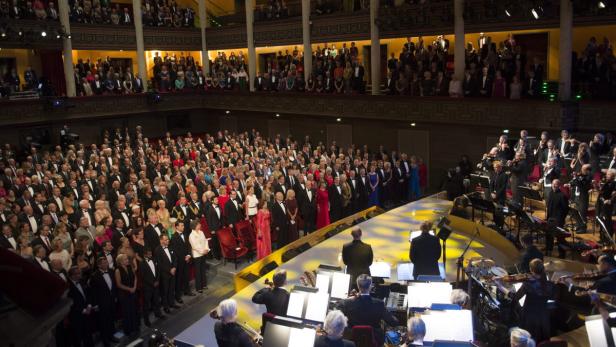 Ein Orchester spielt vor einem großen Publikum in einem Konzertsaal.