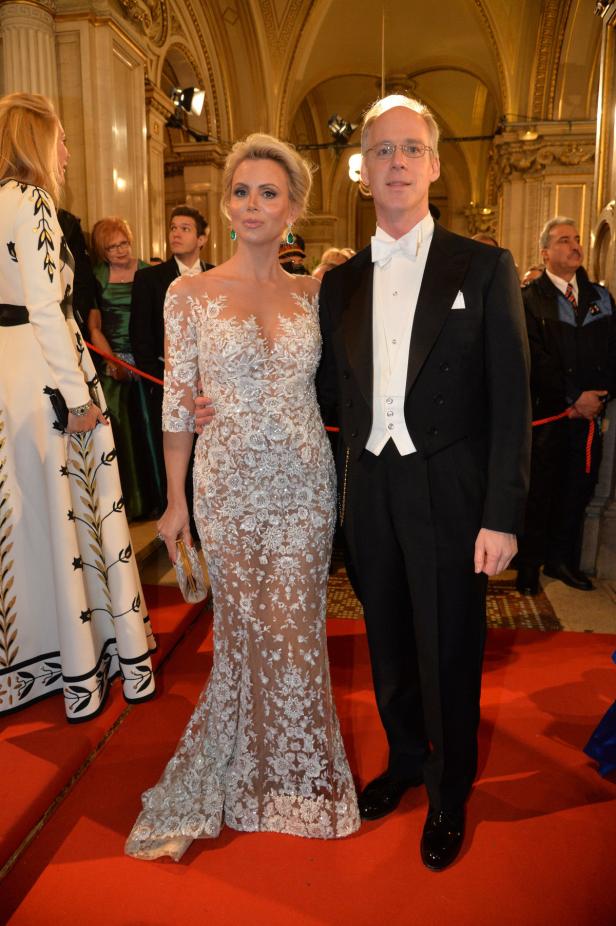 Eine Frau in einem weißen Spitzenkleid und ein Mann im Frack posieren auf einem roten Teppich.