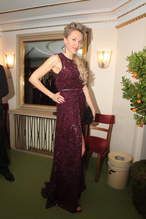 Eine Frau in einem burgunderroten, paillettenbesetzten Abendkleid posiert in einem eleganten Raum.