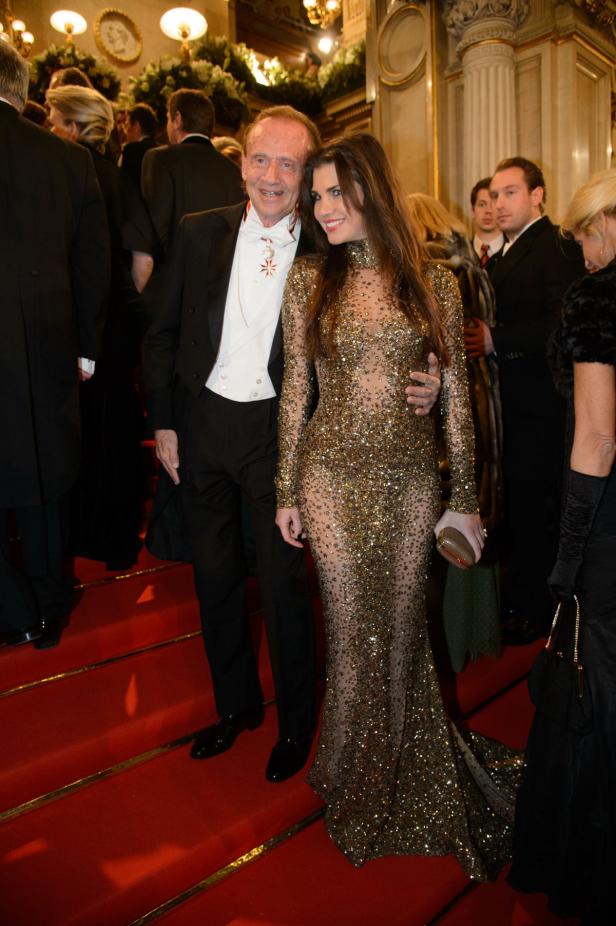 Ein älterer Mann im Smoking mit einer Frau in einem goldenen Paillettenkleid auf einer roten Treppe.