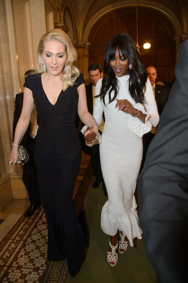 Naomi Campbell in einem weißen Kleid, Hand in Hand mit einer Frau in Schwarz.