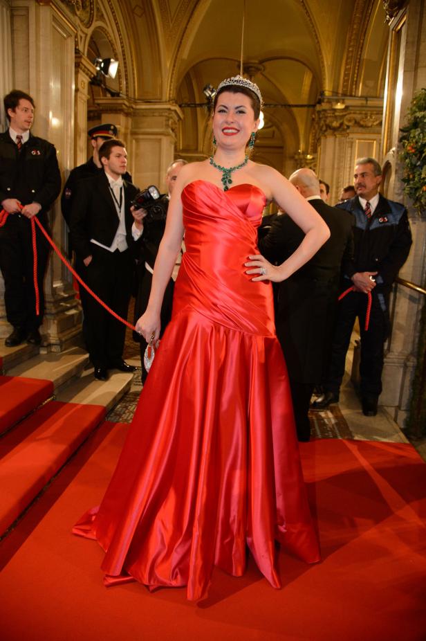 Eine Frau in einem roten Abendkleid und Diadem posiert auf einem roten Teppich.